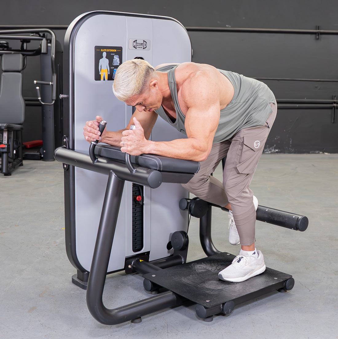 Man using a gray and black glute extension machine in a gym.