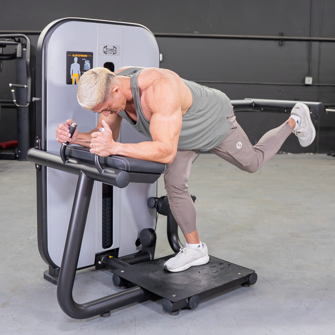 Man using a glute extension machine in a gym, with one leg extended back.