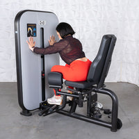 Thumbnail for Woman in red pants using a gray and black inner/outer thigh workout machine.