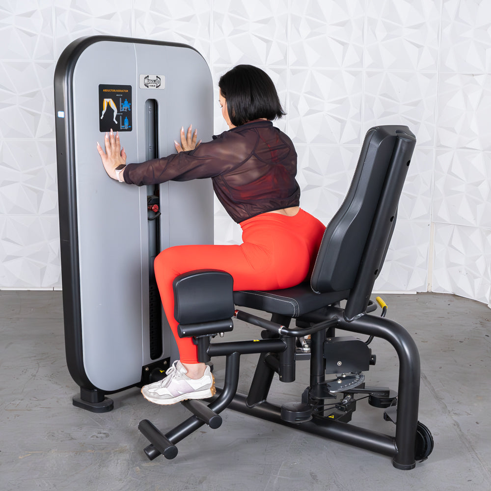 Woman in red leggings using a gray and black inner/outer thigh workout machine.