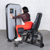 Thumbnail for Woman in red leggings using a gray and black inner/outer thigh workout machine.
