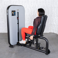 Thumbnail for Woman in red leggings using a gray and black inner/outer thigh workout machine.