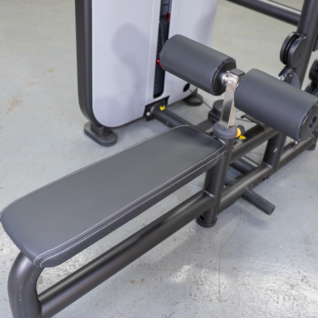 Close-up of a black gym bench with white stitching and leg pads, part of a gray fitness machine.