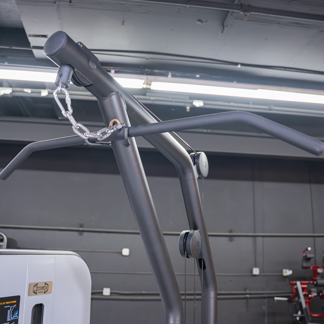Close-up of a lat pulldown bar attached to a gray fitness machine with a chain and carabiner.