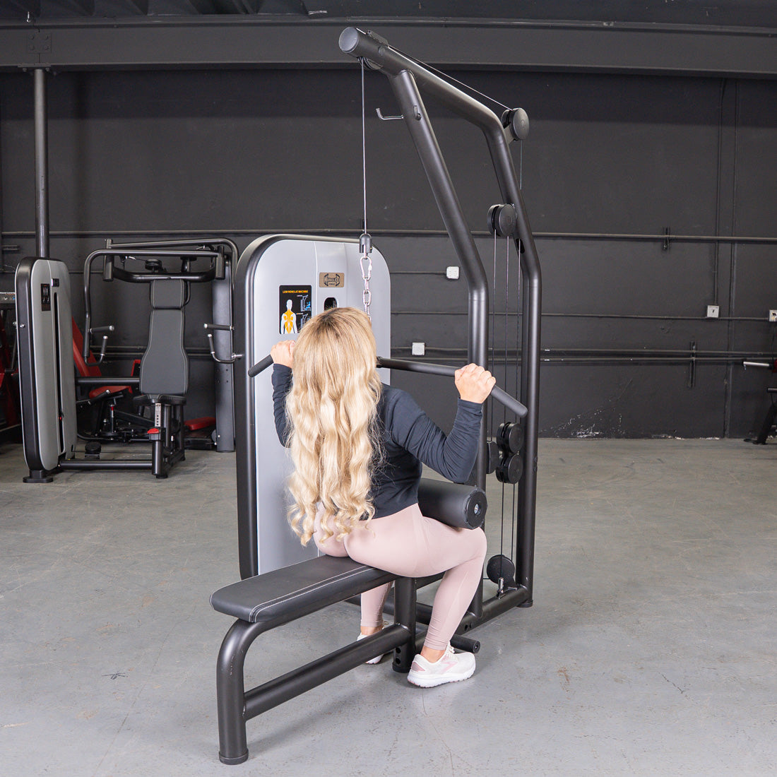 Woman with long blonde hair using a black and gray lat pulldown/low row machine in a gym.