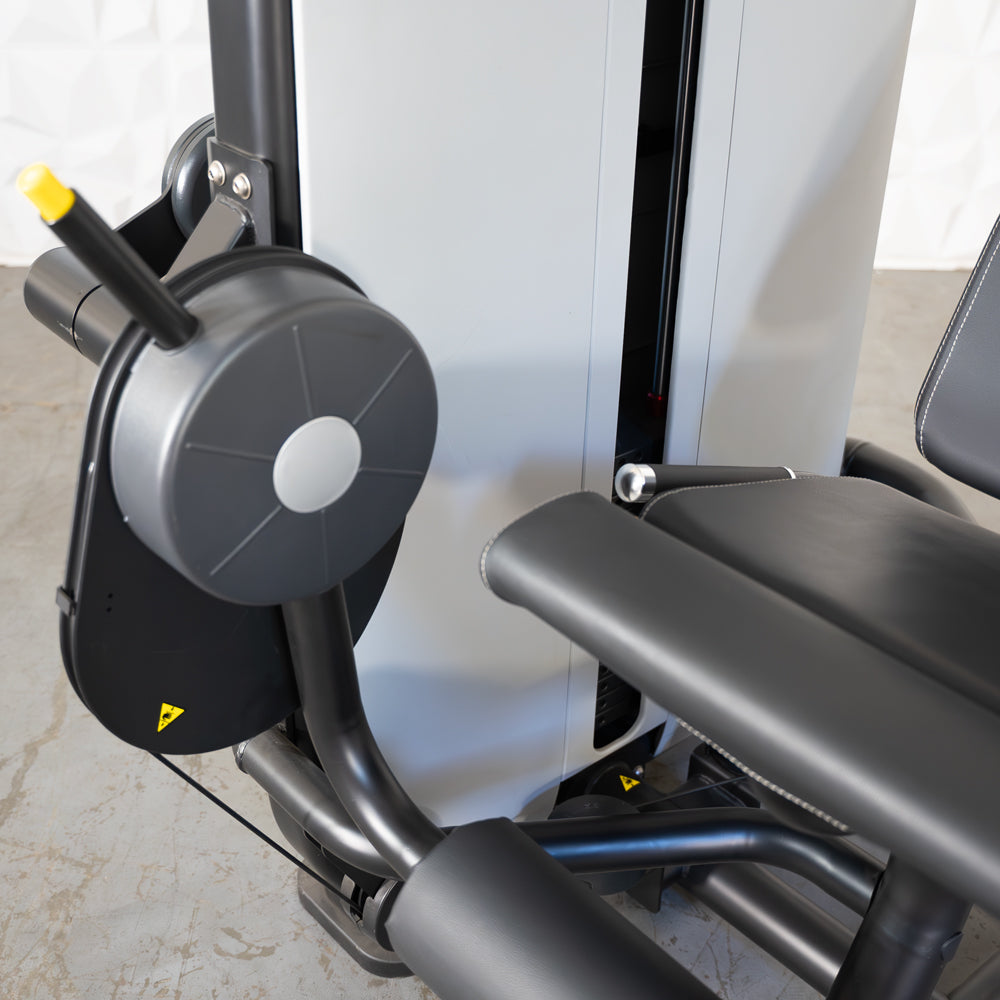 Close-up of a leg extension machine with black padded seat and leg rest, gray weight stack, and adjustment knob.