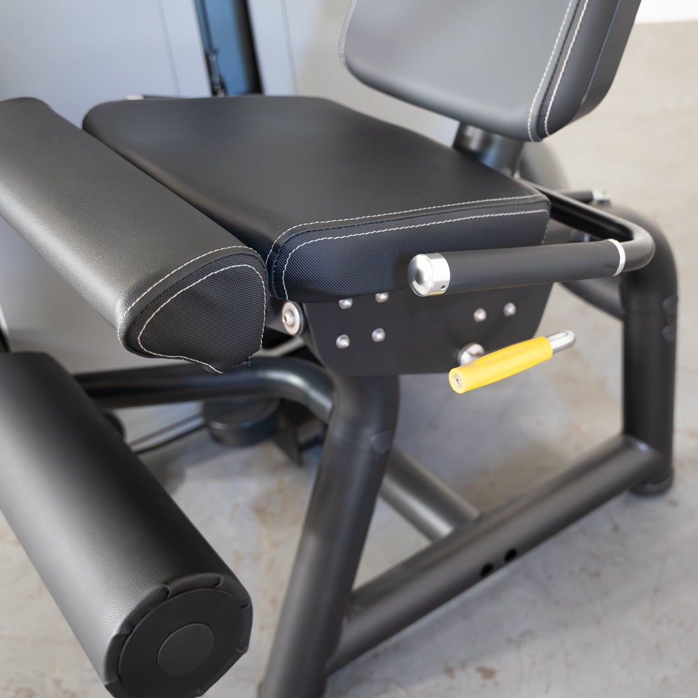 Close-up of a black leg extension machine with white stitching, yellow adjustment handle, and padded rollers.