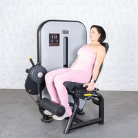 Thumbnail for Woman in pink activewear using a gray and black leg extension machine.