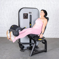 Thumbnail for Woman in pink activewear performing leg extensions on a grey and black fitness machine.