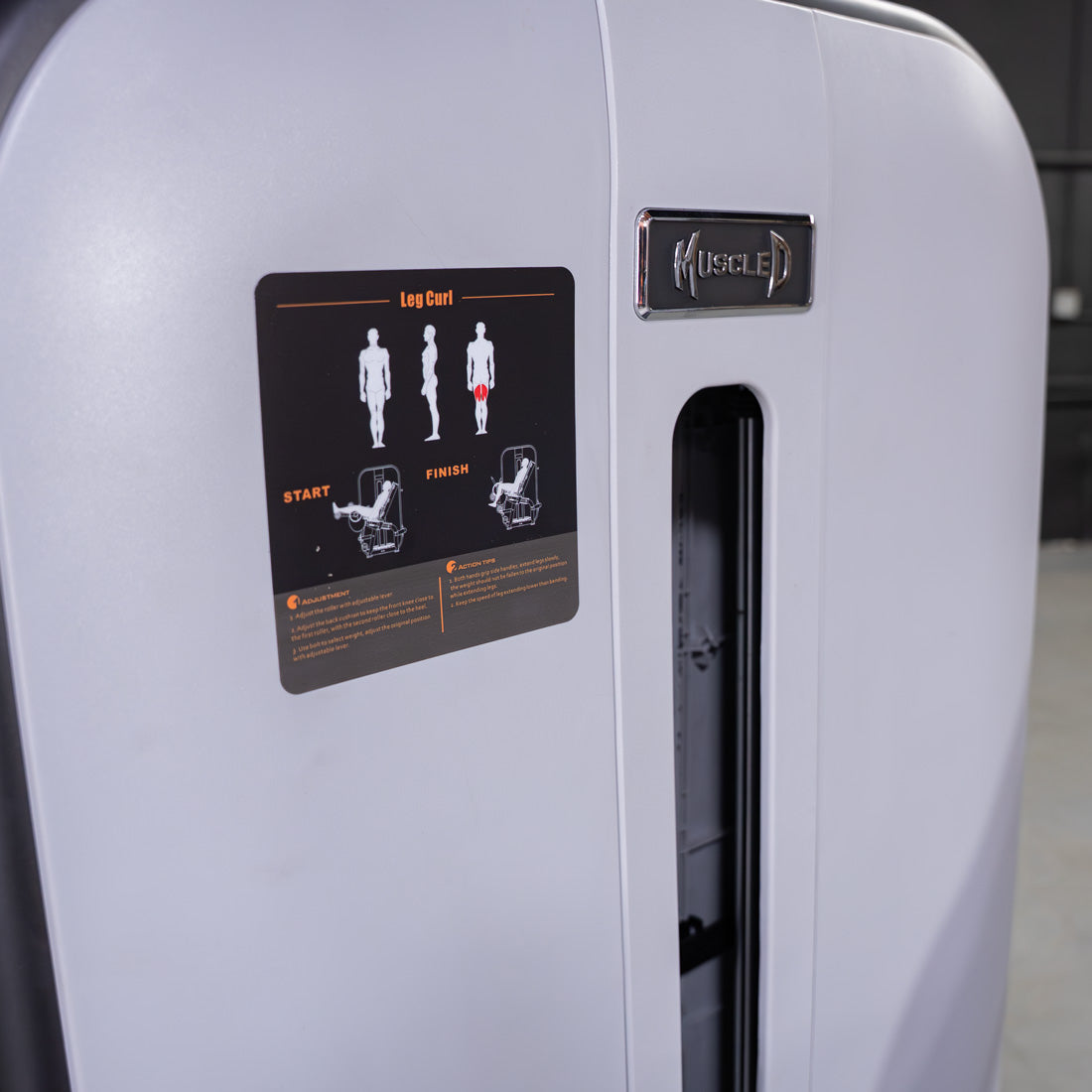Close-up of a leg curl machine with exercise instructions and "MUSCLE D" logo.