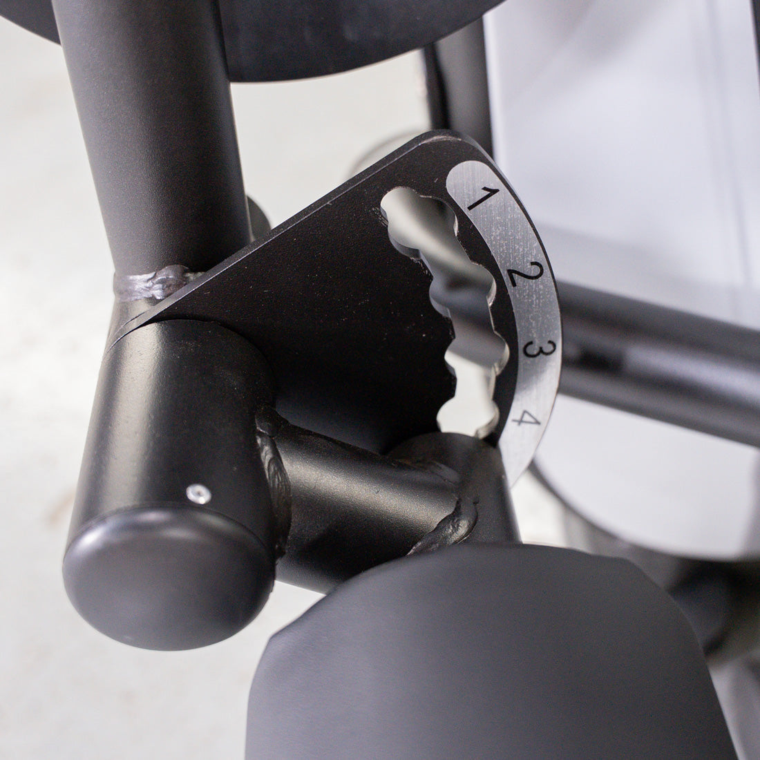 Close-up of a black metal fitness machine adjustment mechanism with numbers 1-4.
