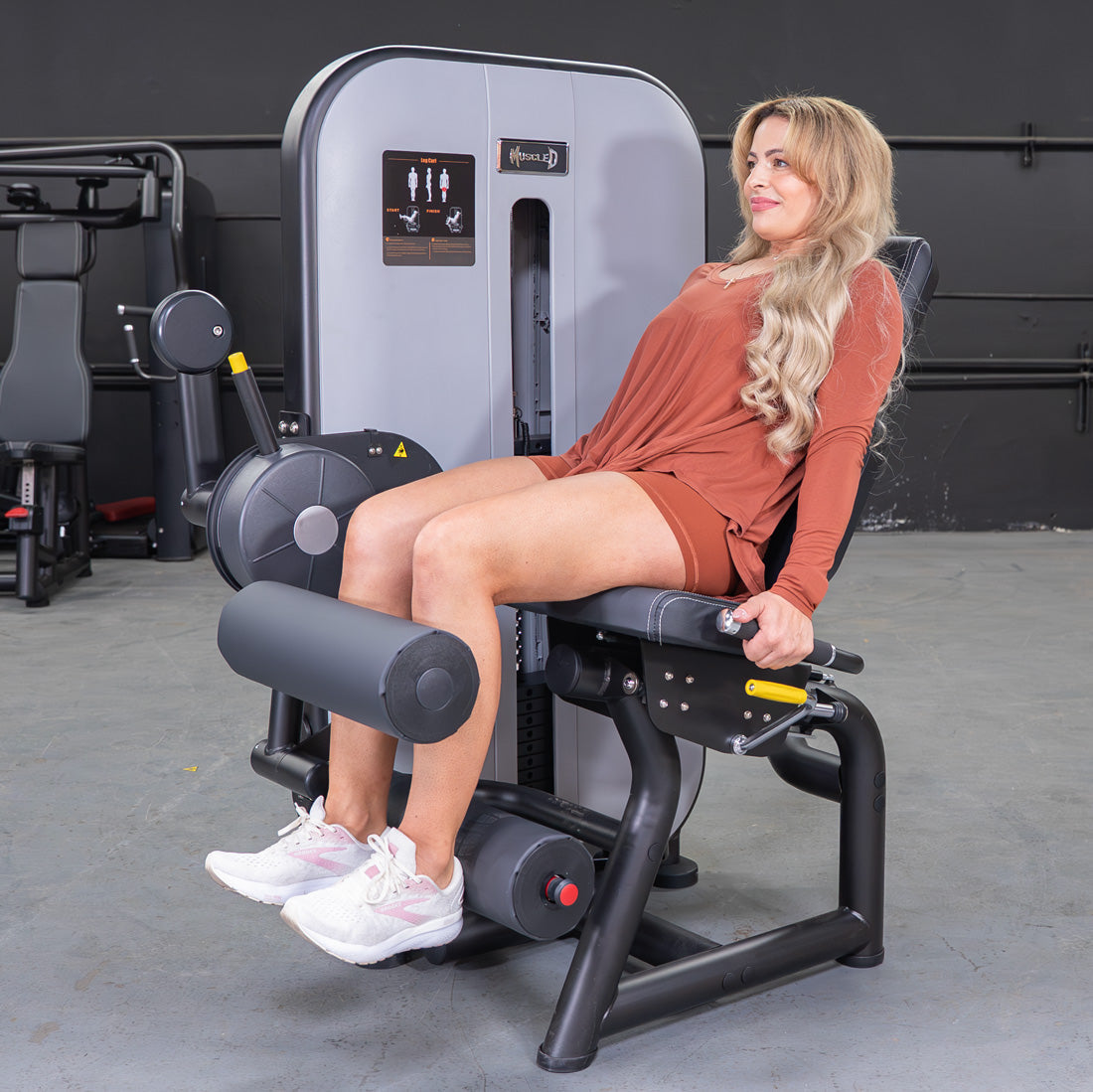 Woman seated on a leg curl machine, performing a hamstring workout.