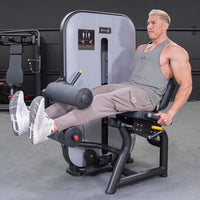 Thumbnail for Man performing a seated leg curl on a gray and black fitness machine.