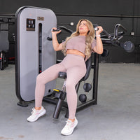 Thumbnail for Woman in a gym using a shoulder press machine with an adjustable seat and pin selectorized weight stack.
