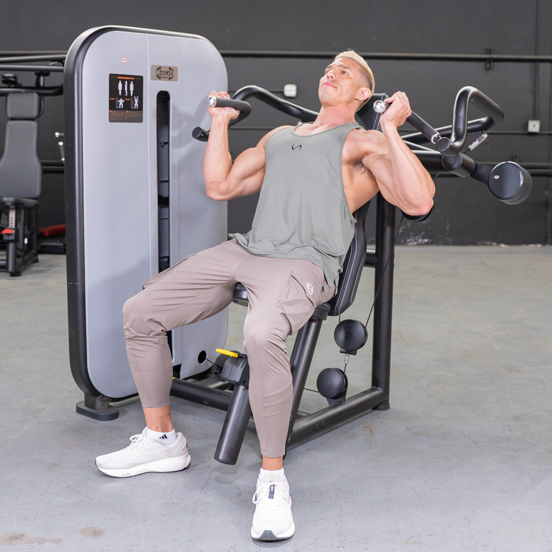 Man using a shoulder press machine with an adjustable seat and pin selectorized weight stack.