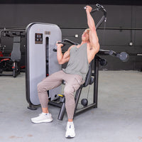 Thumbnail for Man in a gym using a shoulder press machine, pushing one handle up while holding the other.