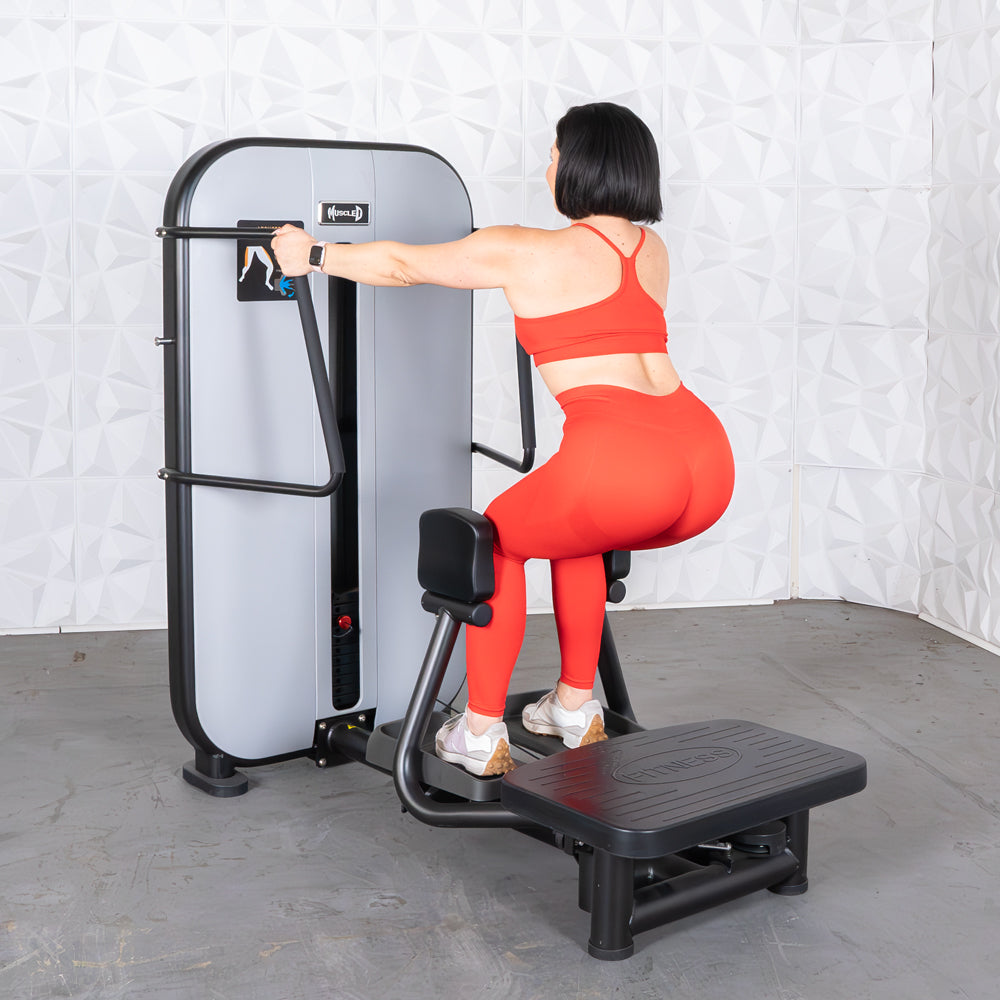 Woman in red using a standing abductor machine, viewed from behind.