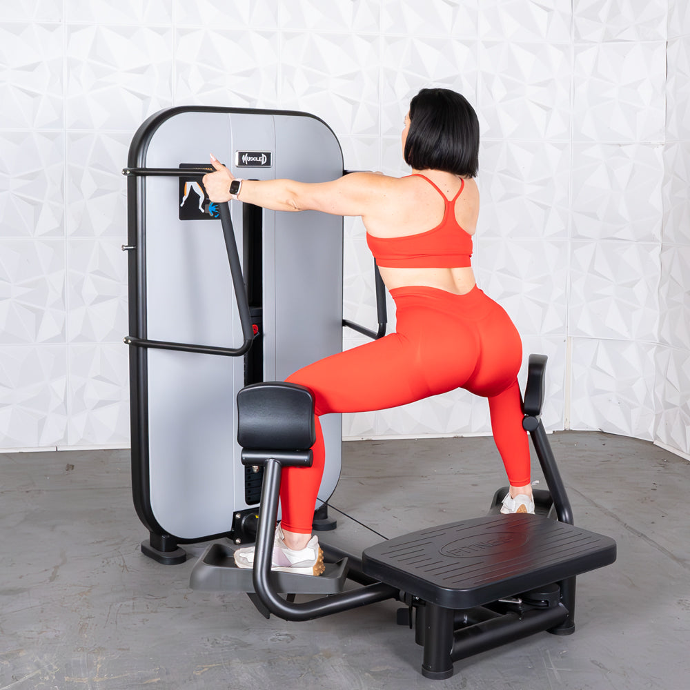 Woman in red using a standing abductor machine, viewed from behind.