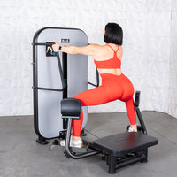 Thumbnail for Woman in red using a standing abductor machine, viewed from behind.