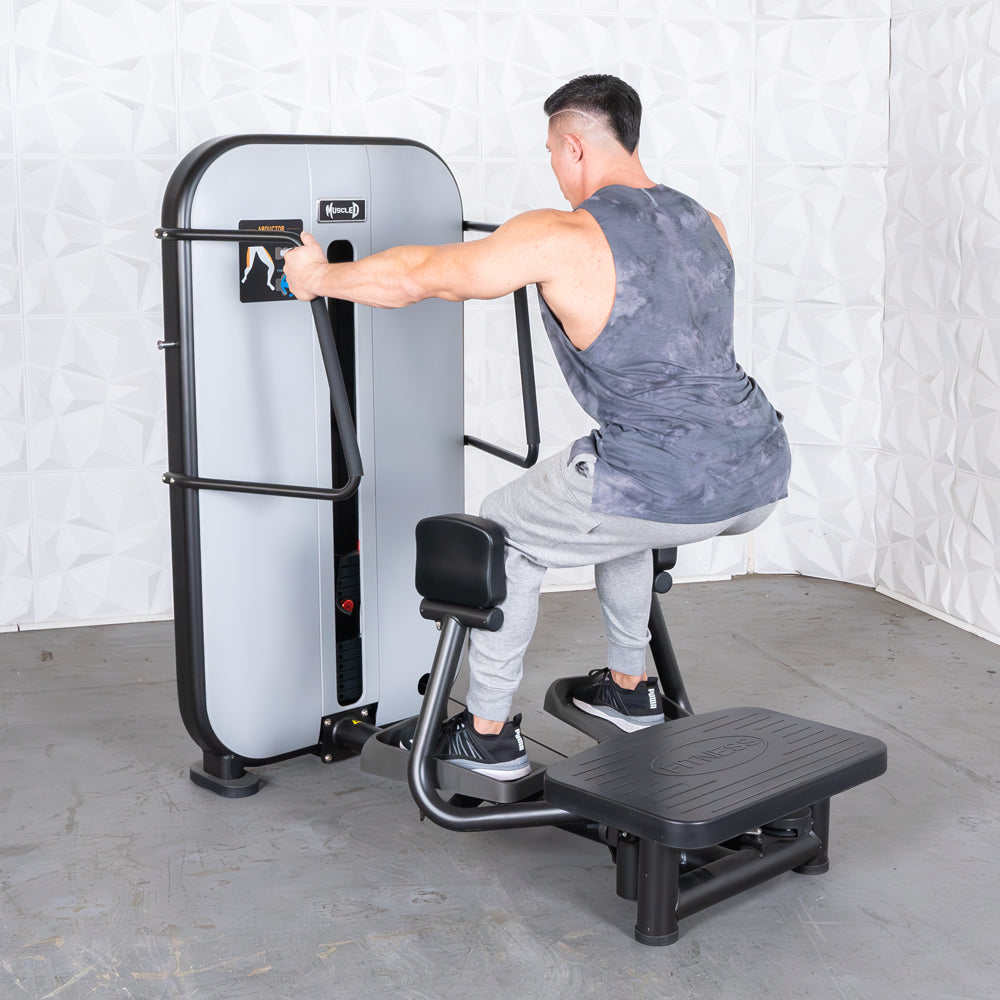 Man using a standing abductor machine, pushing out with his left leg, in a gym setting.