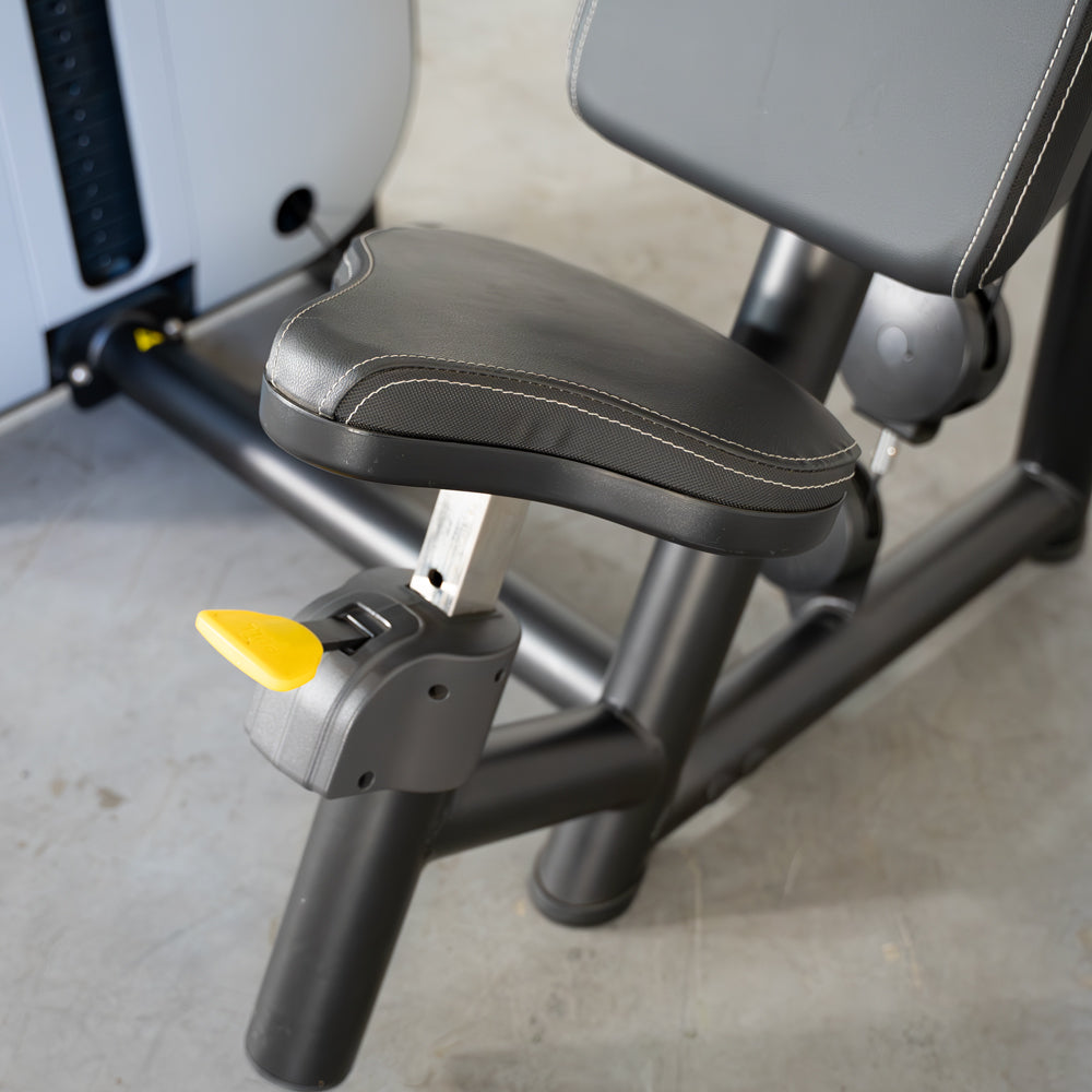 Adjustable black padded seat with white stitching and yellow lever on a triceps extension machine.