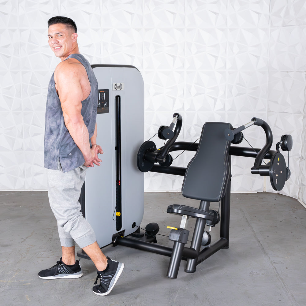Man in tank top stands next to a gray and black triceps extension machine with an adjustable seat.