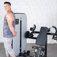 Thumbnail for Man in tank top next to a gray and black triceps extension machine with an adjustable seat.