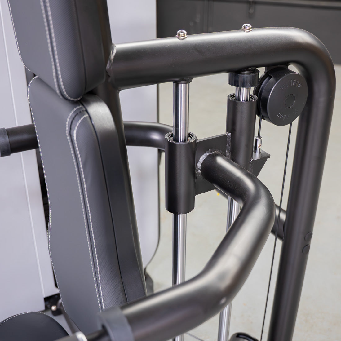 Close-up of a triceps press-down machine with a black padded seat, black frame, and chrome adjustment bars.