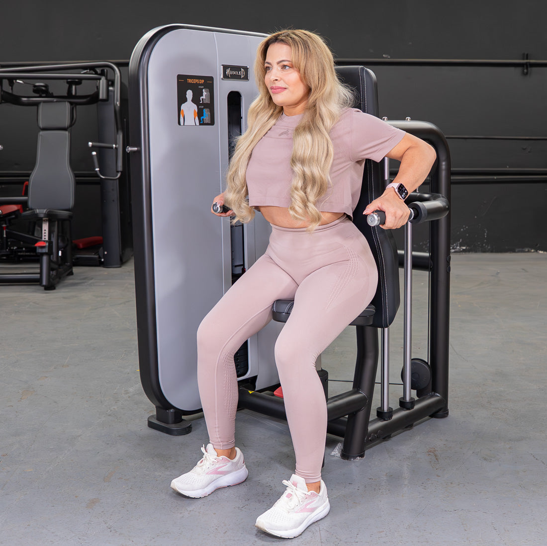 Woman in pink activewear using a triceps press-down machine in a gym.