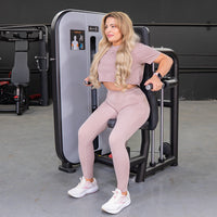 Thumbnail for Woman in pink activewear using a triceps press-down machine in a gym.