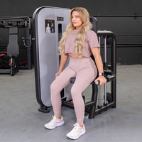 Thumbnail for Woman in pink activewear seated on a triceps press-down machine, holding handles.