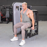 Thumbnail for Man in a tank top and cargo pants using a triceps press-down machine in a gym.