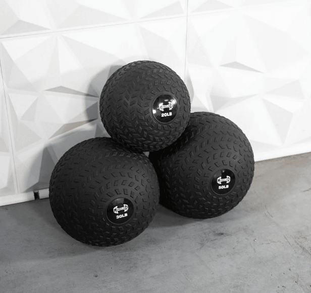 Three black slam balls with textured surfaces and weight labels (20LB, 30LB, 50LB) stacked on a concrete floor.