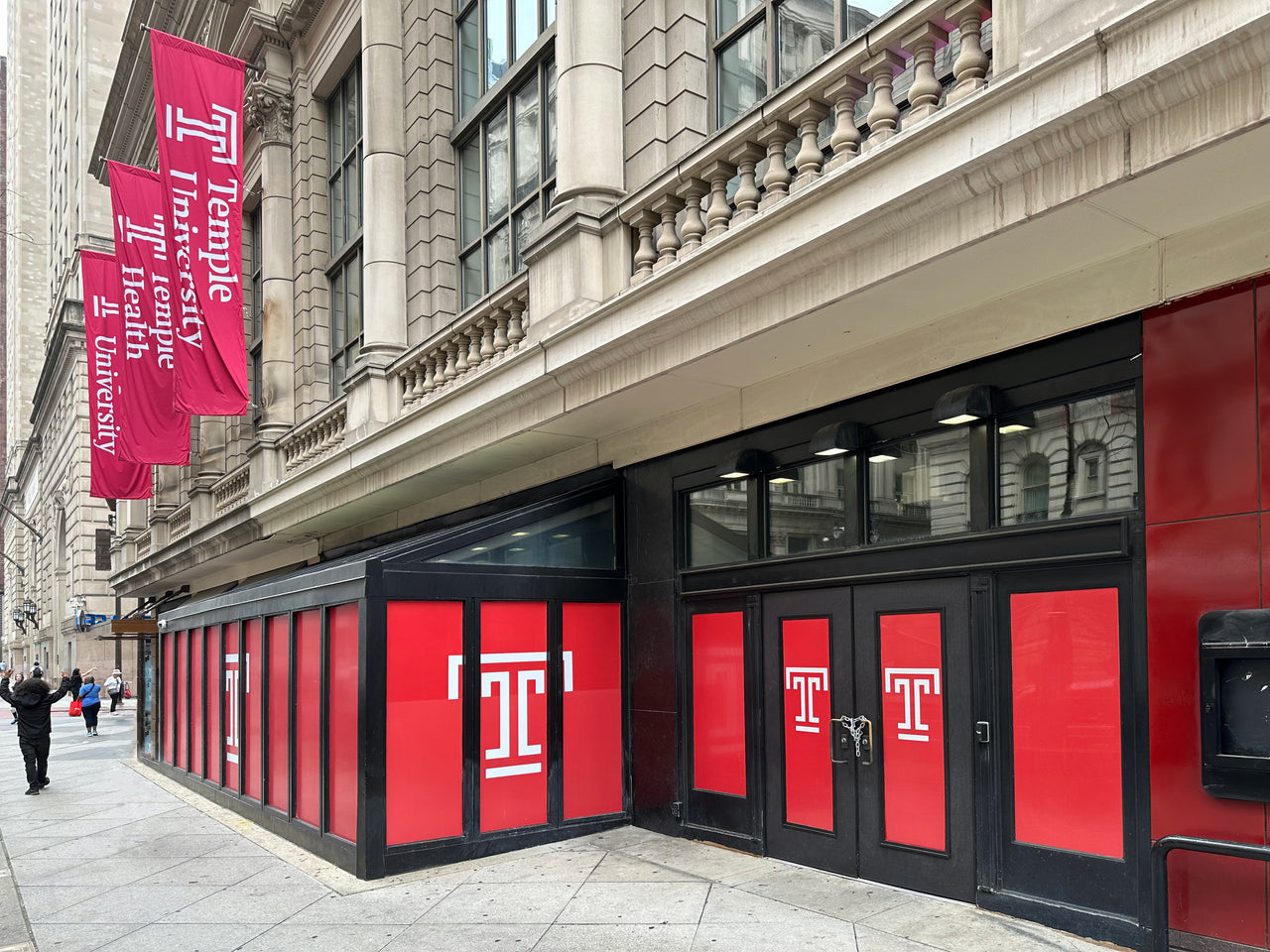 Red window graphics with white Temple T logos on the storefront windows and doors of a stone building