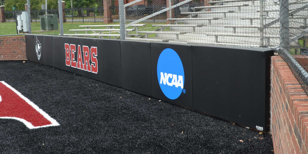 Black folding backstop pads printed with Bears and an NCAA logo along a brick wall
