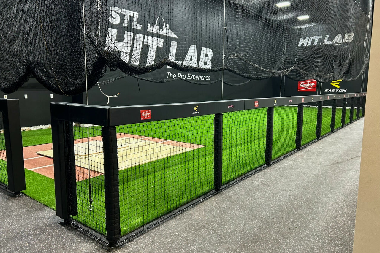 Black square fence rail padding and post pads installed along the perimeter of an indoor batting cage facility