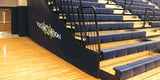 Black bleacher end closure with "Viking Nation" logo next to blue stadium seating and a wooden gym floor.