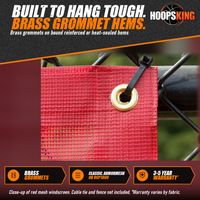 Thumbnail for Close-up of red vinyl-coated mesh windscreen with a brass grommet and black cable tie on a chain-link fence rail