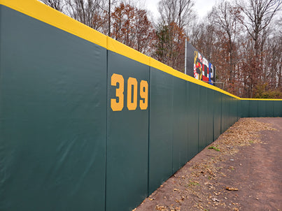 Green and gold stadium outfield wall padding at Prince George's Stadium showing custom distance markers and protective padding for minor league baseball