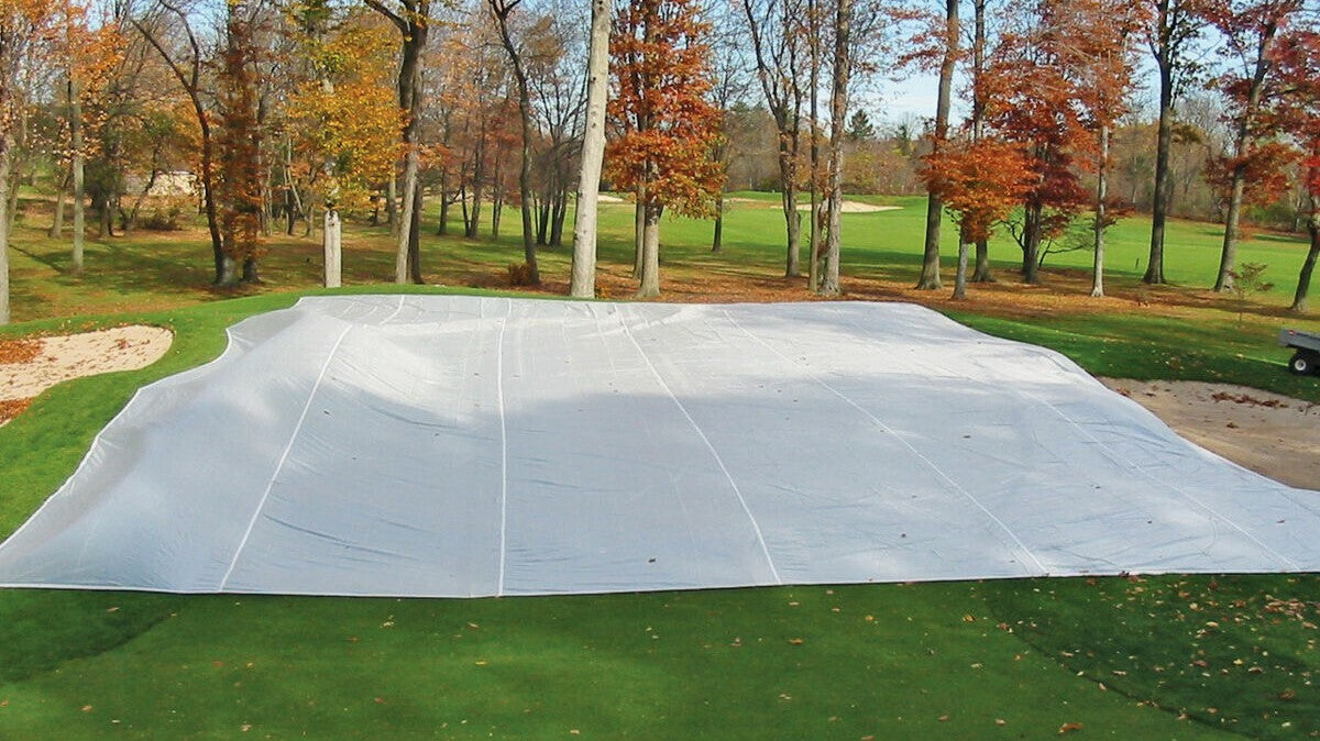 FieldSaver golf course green cover from CoverSports protecting a putting green in late fall, with fall foliage and fairway visible in the background