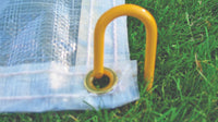 Thumbnail for Close-up of a brass grommet on a FieldSaver golf course cover secured to grass with a yellow turf staple, showing the reinforced hem and grommet hardware included on every CoverSports cover