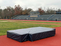 Thumbnail for Dark gray weather cover over a high jump mat on a red track in front of stadium bleachers
