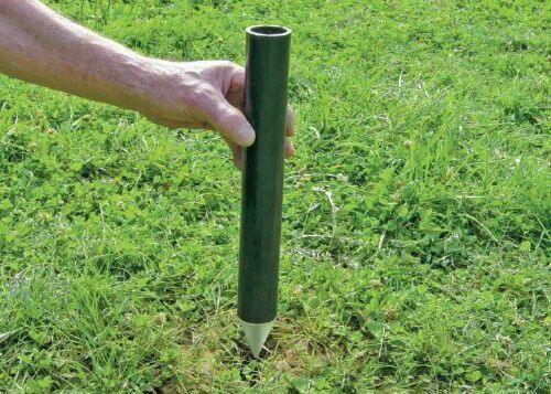 Hand pushing a green fence ground socket with a pointed tip into grass