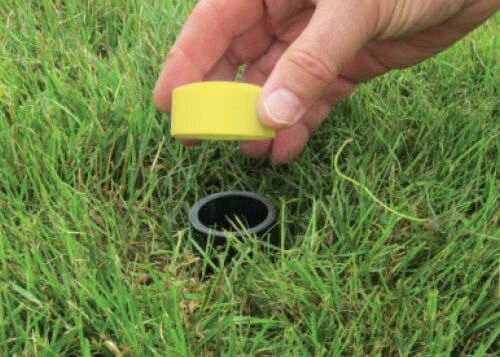 Hand placing a yellow cap over a black fence ground socket set in grass