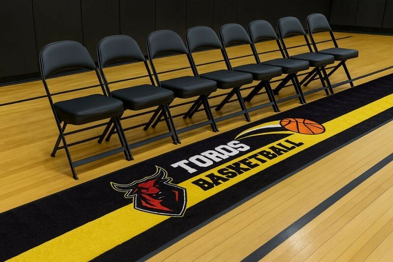 Black and yellow custom logo floor mat reading Toros Basketball with a red bull logo beside a row of bench chairs
