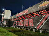 Custom printed black stadium bleacher enclosure featuring Serpentini Stadium branding, team mascot, and sponsor graphics with red and white design at Orrville football stadium under night lights