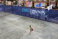 Thumbnail for Tennis player serving in front of custom printed blue tennis fence windscreen featuring ZMG Tennis at Deer Creek branding and facility logos