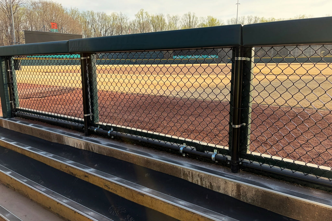 Green dugout rail pads with visible attachment hardware on a baseball stadium fence rail