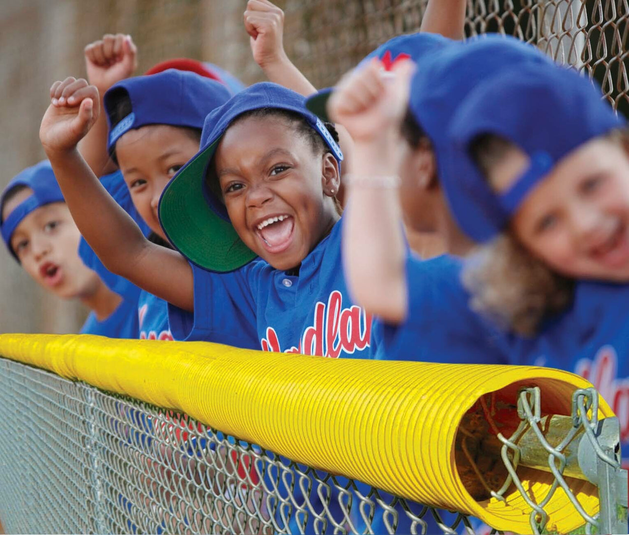 Athletic gold FenceCrown poly topper capping a chain-link outfield fence at a youth baseball field