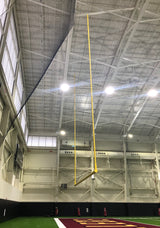 Yellow football goalposts hanging from a high ceiling in an indoor sports facility.
